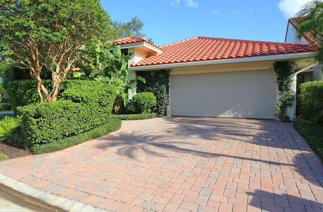 mediterranean / spanish home featuring a garage, a tile roof, decorative driveway, and stucco siding