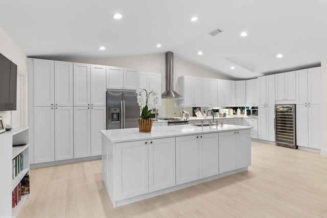 kitchen with wine cooler, stainless steel refrigerator with ice dispenser, light countertops, a sink, and wall chimney range hood