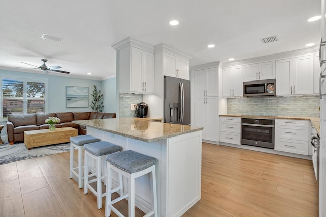 kitchen with stainless steel appliances, a kitchen bar, visible vents, and white cabinets