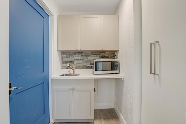 kitchen featuring wood finished floors, a sink, light countertops, tasteful backsplash, and stainless steel microwave