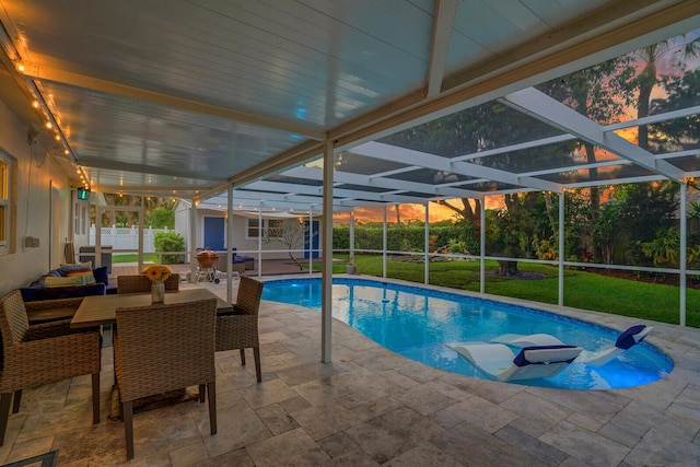 pool at dusk featuring a yard, a patio area, fence, and a lanai