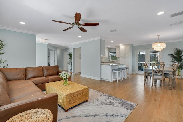 living room featuring light wood-style floors, baseboards, visible vents, and crown molding