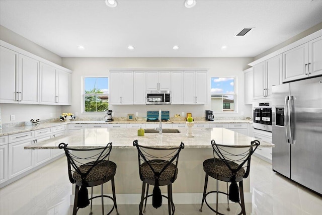 kitchen featuring visible vents, a center island with sink, appliances with stainless steel finishes, and a wealth of natural light