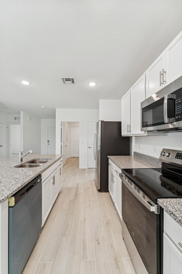 kitchen featuring appliances with stainless steel finishes, white cabinets, a sink, and light stone counters