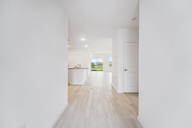 corridor with light wood finished floors, baseboards, a sink, and recessed lighting