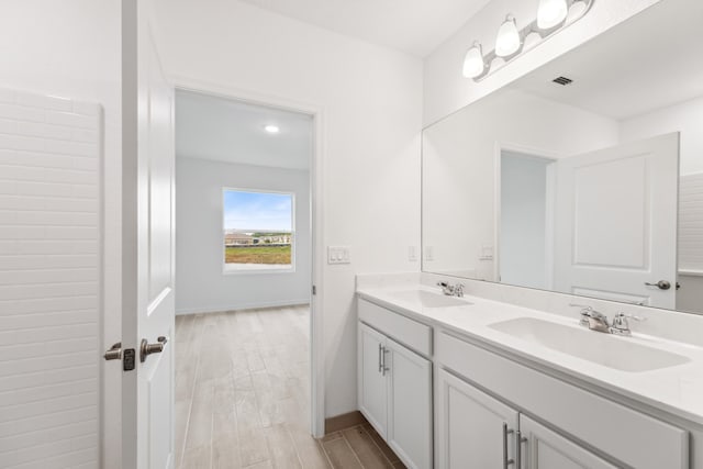 full bathroom featuring double vanity, visible vents, a sink, and wood finished floors