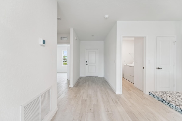 hall featuring visible vents, independent washer and dryer, light wood-style flooring, and baseboards