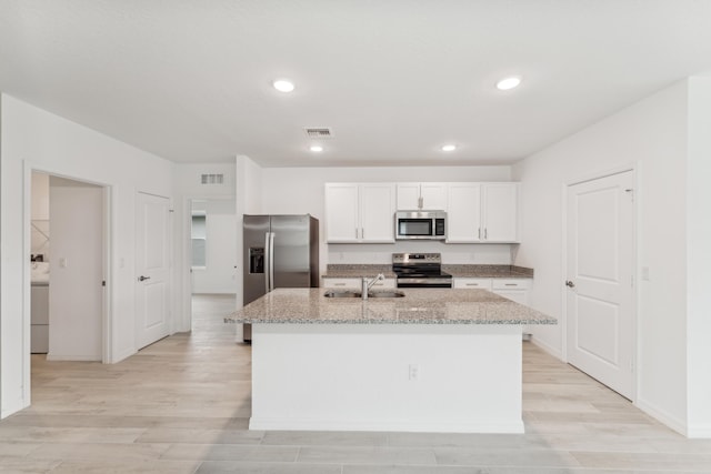 kitchen featuring stainless steel appliances, white cabinets, light stone countertops, washer / clothes dryer, and a center island with sink