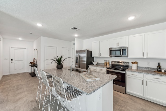 kitchen featuring white cabinets, a kitchen bar, a kitchen island with sink, and stainless steel appliances