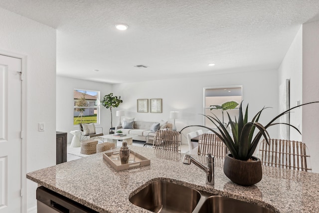 kitchen with light stone counters, stainless steel dishwasher, open floor plan, a sink, and a textured ceiling