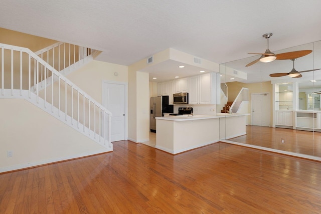 kitchen with a peninsula, light wood-style floors, open floor plan, white cabinets, and appliances with stainless steel finishes