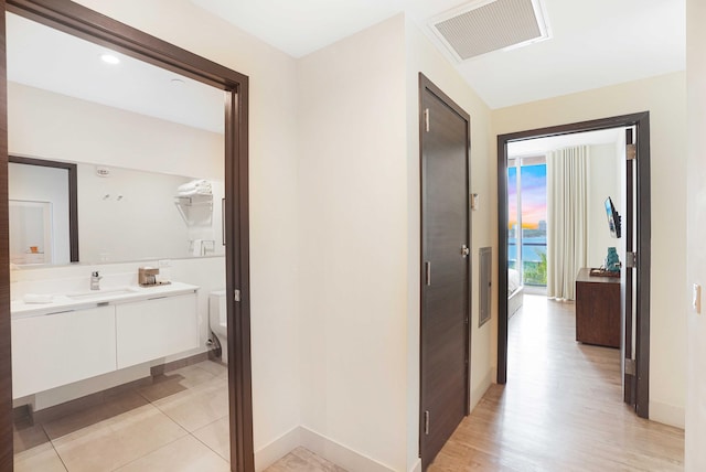 corridor with baseboards, visible vents, a sink, and light tile patterned flooring