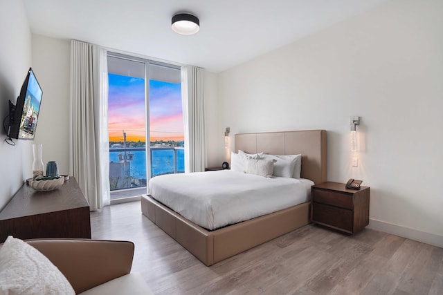 bedroom with light wood finished floors, baseboards, a water view, access to exterior, and floor to ceiling windows