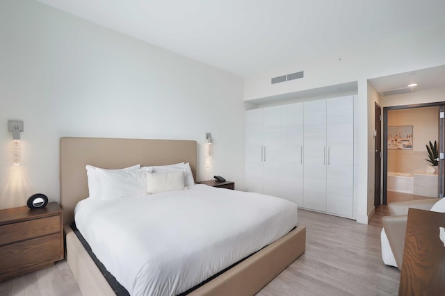 bedroom featuring light wood-style floors, visible vents, a closet, and ensuite bathroom