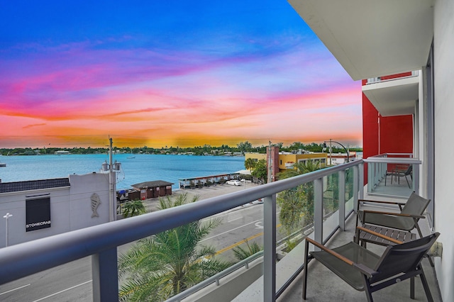 balcony at dusk featuring a water view