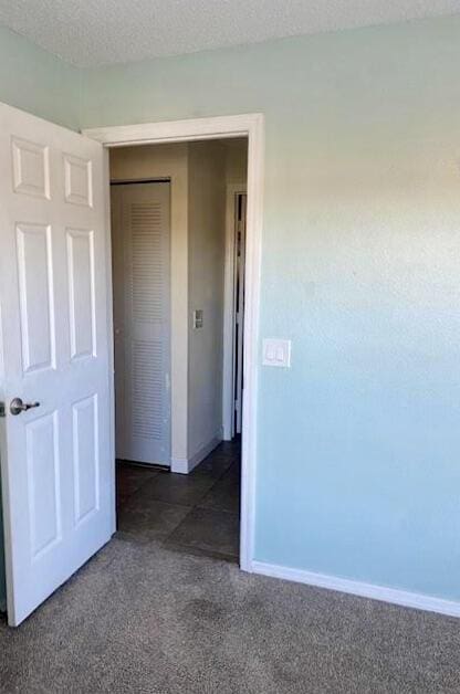 unfurnished bedroom with a closet, dark carpet, a textured ceiling, and baseboards