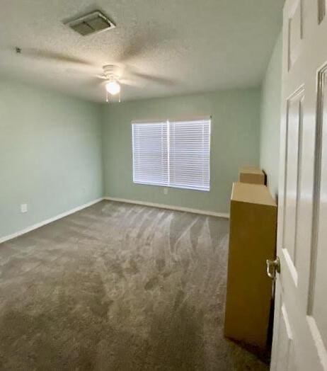 unfurnished room with a textured ceiling, dark colored carpet, visible vents, and baseboards