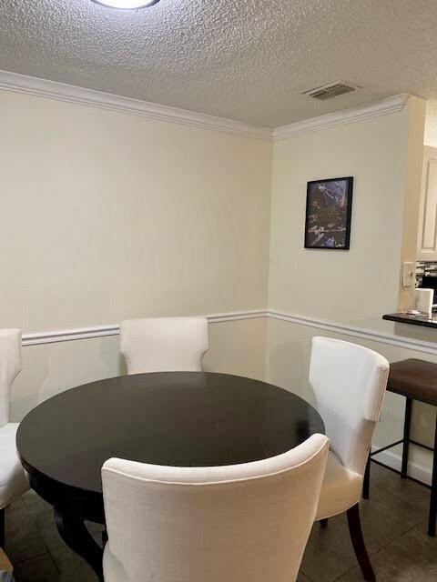 dining space with a textured ceiling, visible vents, and crown molding