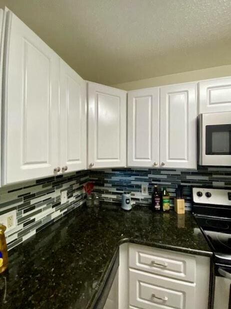 kitchen featuring electric range, dark stone counters, white cabinets, and decorative backsplash