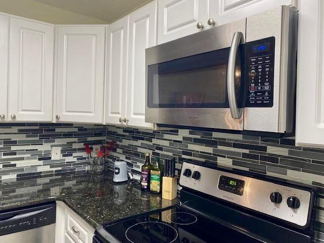 kitchen featuring appliances with stainless steel finishes, dark stone countertops, white cabinetry, and decorative backsplash