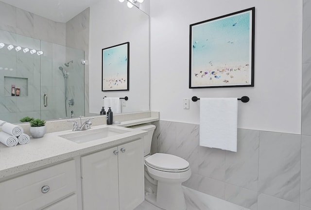 bathroom featuring tile walls, wainscoting, vanity, toilet, and a marble finish shower