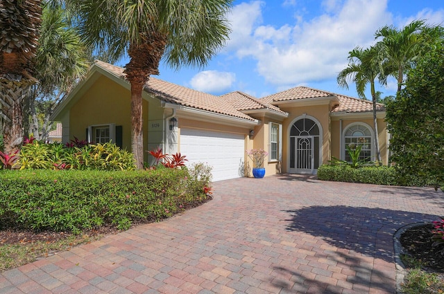 mediterranean / spanish house featuring a garage, a tile roof, decorative driveway, and stucco siding