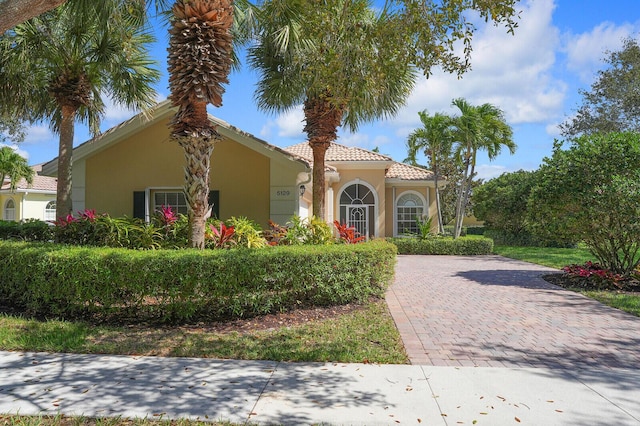 mediterranean / spanish home featuring a tiled roof, decorative driveway, and stucco siding