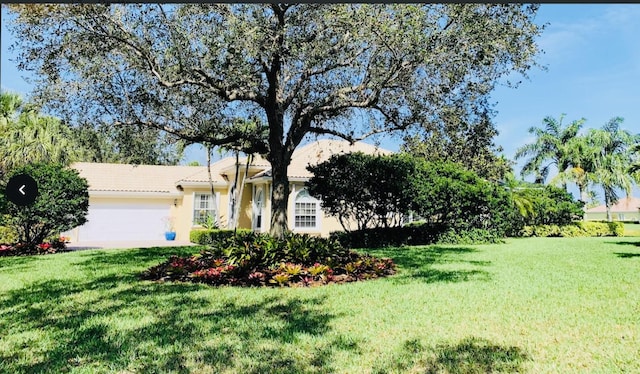 view of front of property featuring an attached garage, stucco siding, a tile roof, and a front lawn