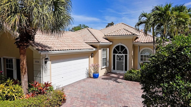 mediterranean / spanish house featuring a tiled roof, decorative driveway, an attached garage, and stucco siding