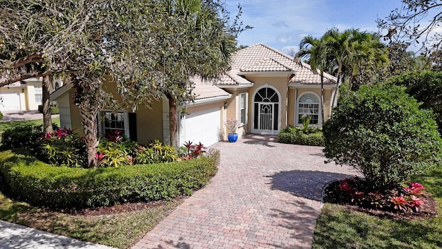 mediterranean / spanish-style home featuring a tiled roof, decorative driveway, an attached garage, and stucco siding