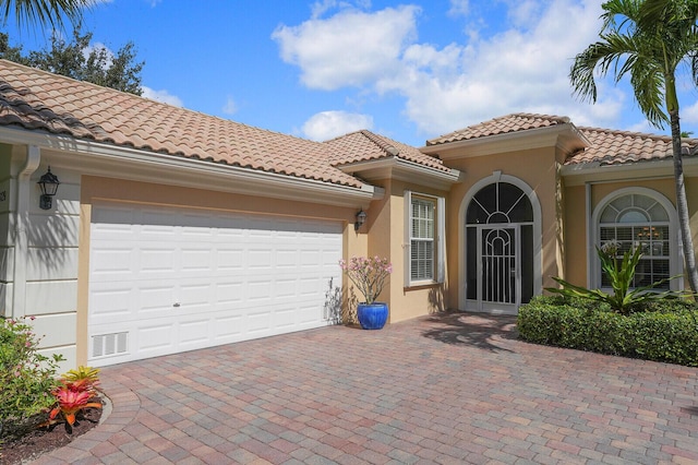 property entrance with decorative driveway, a tile roof, stucco siding, visible vents, and a garage