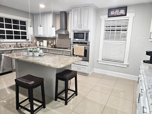 kitchen with light stone counters, a kitchen bar, backsplash, appliances with stainless steel finishes, and wall chimney exhaust hood