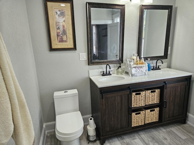 bathroom featuring wood finished floors, a sink, toilet, and double vanity