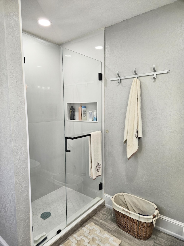 bathroom featuring a textured wall, a shower stall, baseboards, and wood finished floors