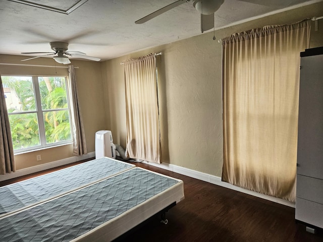 unfurnished bedroom featuring a ceiling fan, baseboards, wood finished floors, and a textured wall