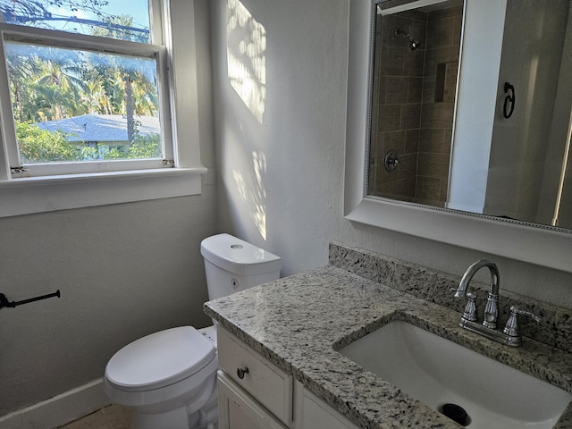 bathroom featuring tiled shower, vanity, toilet, and baseboards