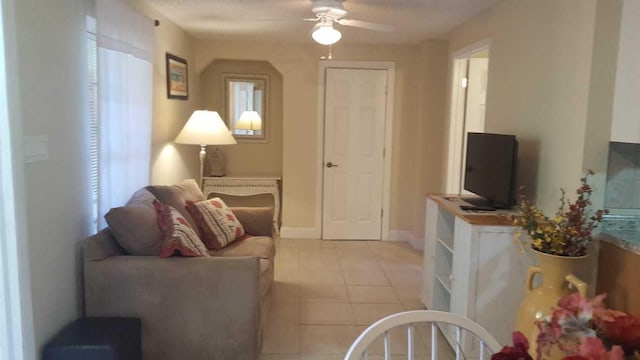 living area featuring light tile patterned flooring, ceiling fan, and baseboards