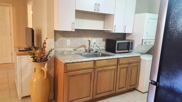 kitchen with stacked washer and dryer, tasteful backsplash, stainless steel microwave, brown cabinets, and a sink