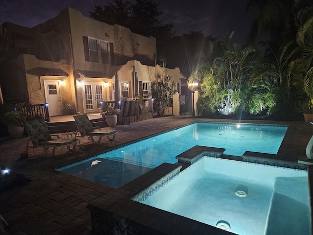 pool at twilight with a pool with connected hot tub, a deck, a patio, and french doors