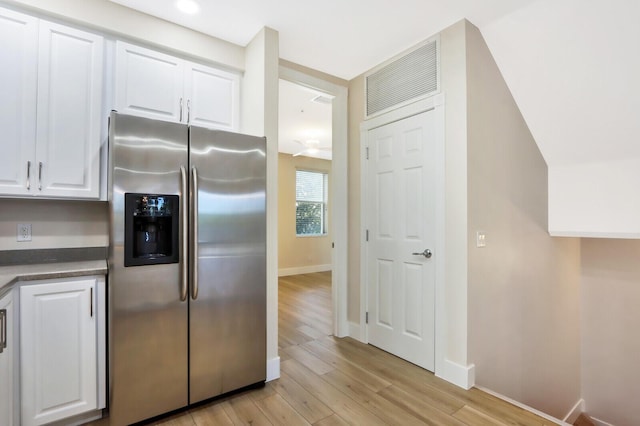 kitchen featuring light wood finished floors, dark countertops, white cabinets, stainless steel fridge, and baseboards