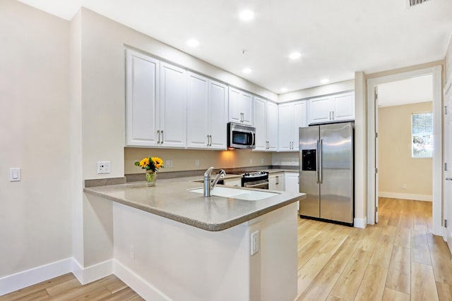 kitchen featuring stainless steel appliances, white cabinetry, a sink, and a peninsula