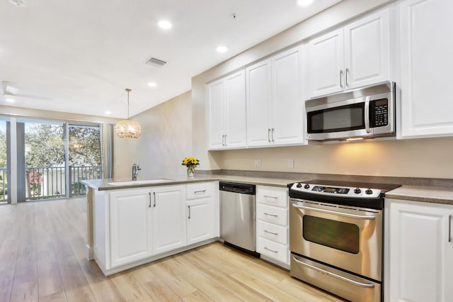 kitchen with white cabinets, a peninsula, stainless steel appliances, pendant lighting, and a sink