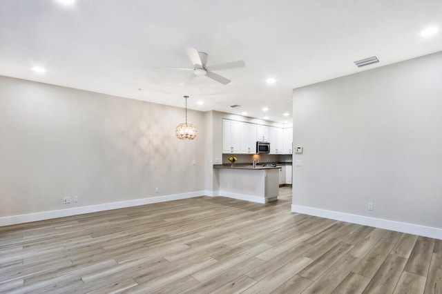 unfurnished living room featuring ceiling fan with notable chandelier, baseboards, light wood-style flooring, and recessed lighting