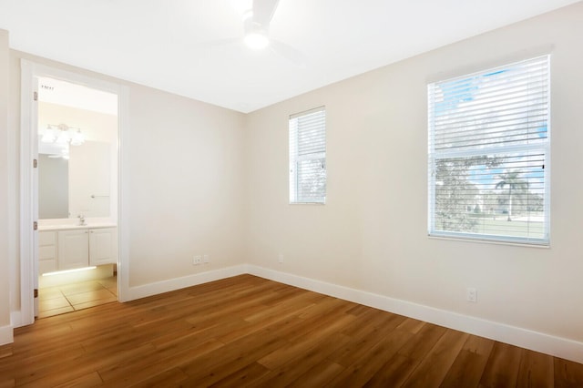 unfurnished bedroom featuring a sink, connected bathroom, baseboards, and wood finished floors