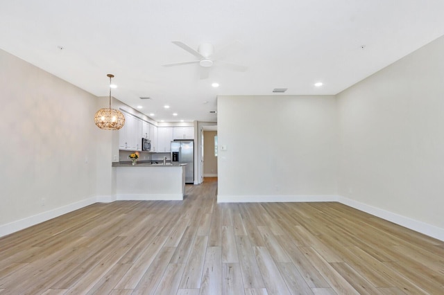 unfurnished living room with light wood-type flooring, baseboards, and ceiling fan with notable chandelier