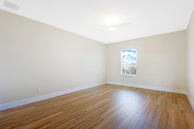 spare room featuring light wood finished floors, a ceiling fan, visible vents, and baseboards