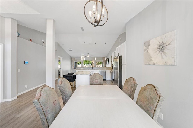 dining space with light wood-type flooring, lofted ceiling, baseboards, and an inviting chandelier