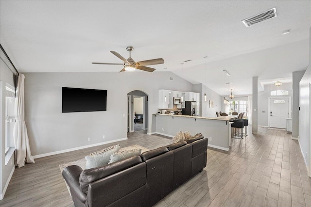 living room with arched walkways, visible vents, vaulted ceiling, ceiling fan, and light wood-type flooring