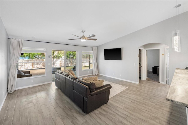 living room with baseboards, arched walkways, a ceiling fan, vaulted ceiling, and light wood-style floors