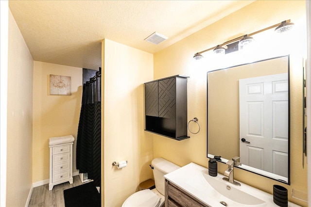 bathroom with a textured ceiling, toilet, wood finished floors, visible vents, and vanity